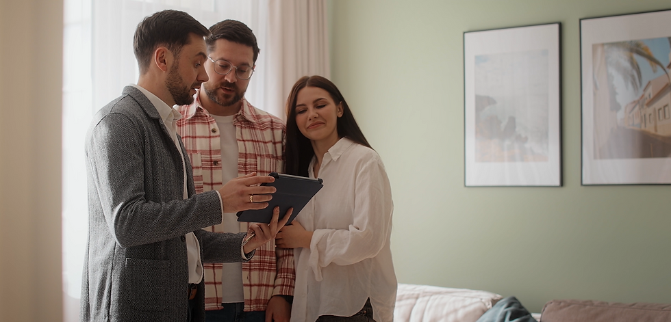 Three adults huddle over a tablet in a softly lit living room, discussing something with focused, pleased expressions.